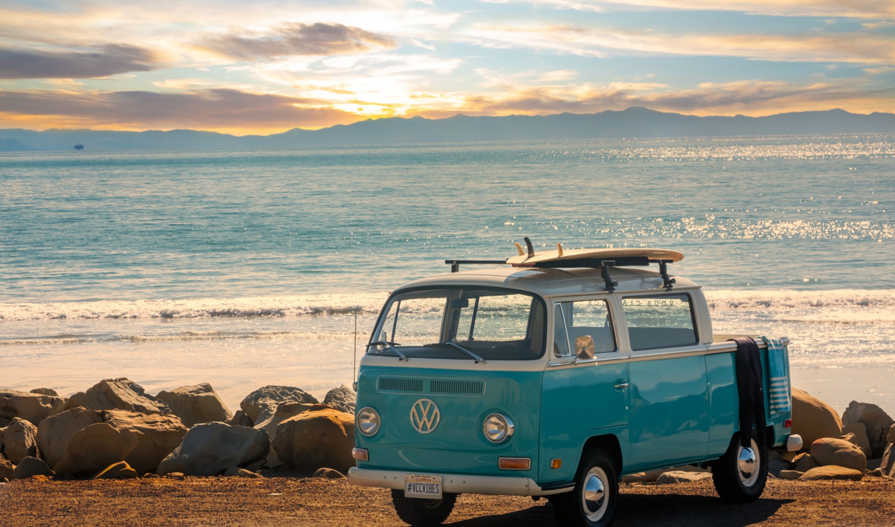 lifestyle image of a bus parked in the gravel beside a bright beach at sunset